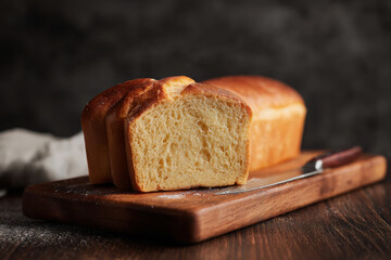 Sliced bread on a dark wooden board with a knife and cloth, ideal for rustic food blogs or bakery menus, or food packaging designs.