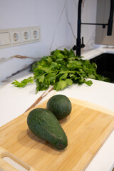 Two Avocados on Cutting Board in Kitchen with Celery Leaves