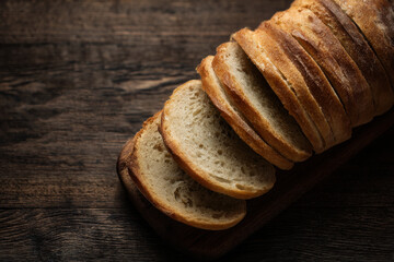 Sliced bread on a dark wooden board with a knife and cloth, ideal for rustic food blogs or bakery menus, or food packaging designs.