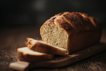Sliced bread on a dark wooden board with a knife and cloth, ideal for rustic food blogs or bakery menus, or food packaging designs.