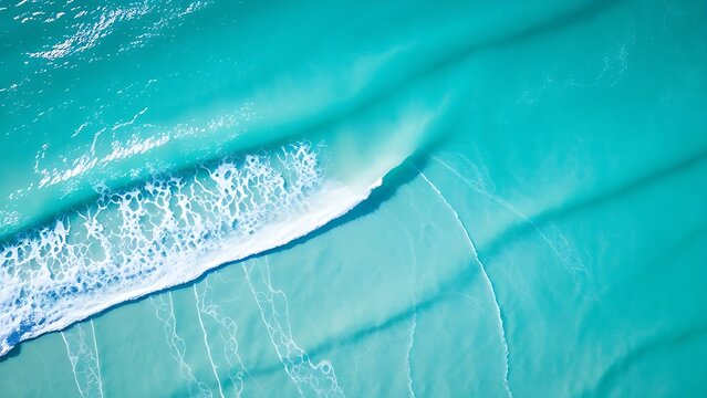 Aerial view of turquoise waves meeting white sand, creating abstract patterns under morning sunlight.
