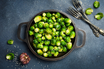 Baked Brussels sprouts with sesame and garlic in a frying pan. Top view, close-up. On a dark textured background. © Yaruniv-Studio