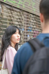 A woman with long hair and a man with a backpack are standing next to each other. The woman is looking at the man with a frown on her face