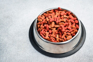 Dry pet food in a bowl. Top view, on a gray stone background.