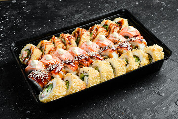 Big set of Sushi rolls with cheese and fish and caviar, Japanese food. Delivery. Disposable tableware. On a black stone background.