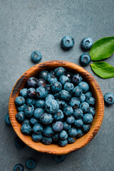 Wooden bowl with fresh blueberries. Close-up, free space for text. On a stone background.