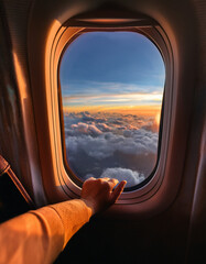 POV from airplane seat, hand resting on the window frame, view of clouds and sunset horizon, dreamy atmosphere, warm glowing tones, minimalist travel aesthetic