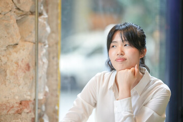 Fototapeta premium A woman is sitting at a table with her hands on her lap. She is wearing a white shirt and has her head tilted to the side. Concept of contemplation and introspection