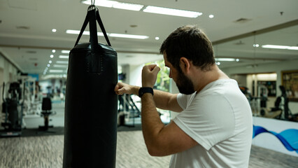 Man in white t-shirt training with a punching bag at the gym, practicing boxing stance and punches with focus and determination during workout session.