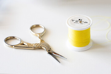 A bright yellow spool of polyester thread sits beside a pair of elegant, antique-style silver scissors on a clean white surface. Perfect for sewing, embroidery, or craft projects.