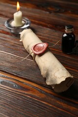 Old rolled scroll, burning candle and inkwell on wooden table, closeup