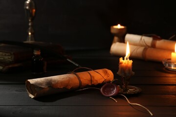Many old rolled scrolls and burning candles on black wooden table, closeup