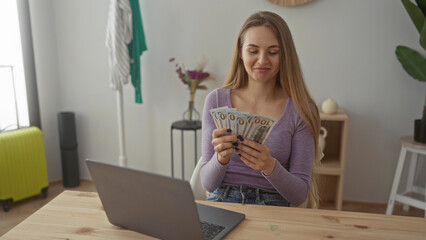 Woman smiling while counting us dollars in bright living room with laptop on wooden table suggesting financial success and home comfort