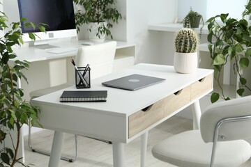 Stylish workplace with laptop, stationery and floral decor in office. Biophilic interior design