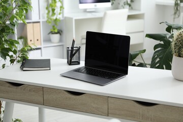 Stylish workplace with laptop, stationery and floral decor in office. Biophilic interior design