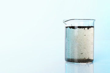 Glass beaker with dirty water on mirror surface, space for text