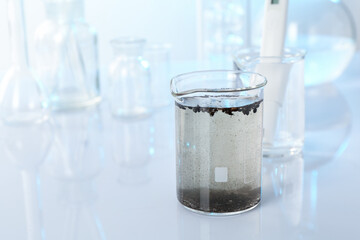 Glass beaker with dirty water, other glassware and digital pH meter on mirror surface, closeup. Space for text