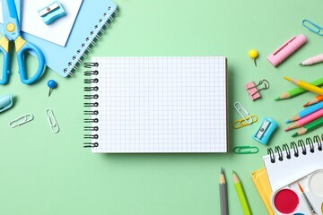 Open notebook with school stationery on green background, top view
