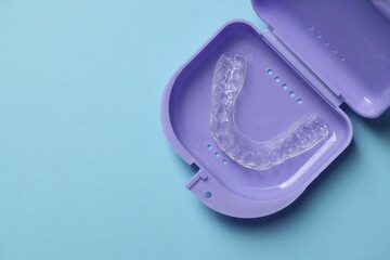One clear aligner in retainer case on light blue background, top view. Space for text