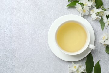 Cup of hot tea with jasmine flowers on gray background, close up