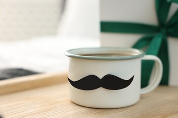 Happy Father's Day. Cup with mustache and gift on bed at home, closeup. Space for text