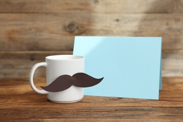Happy Father's Day. Cup with mustache and card on wooden table. Space for text