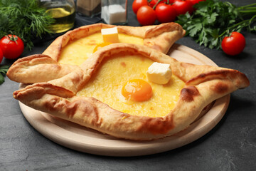 Tasty khachapuri with cheese, egg and other products on black table, closeup