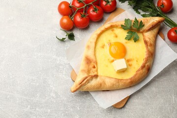 Tasty khachapuri with cheese, egg, parsley and other products on light grey background, flat lay. Space for text