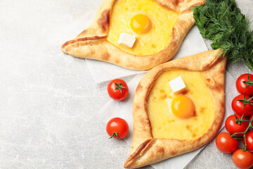 Tasty khachapuri with cheese, egg and other products on light grey background, flat lay. Space for text