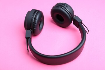 Pair of stylish black headphones on pink background