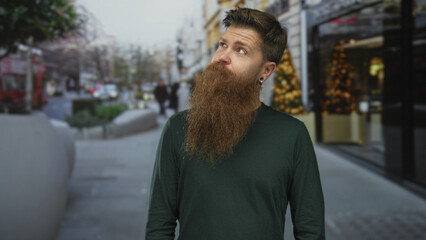 Fototapeta premium Man with long ginger beard looks up at sky on a busy city street with blurred background; curiosity.