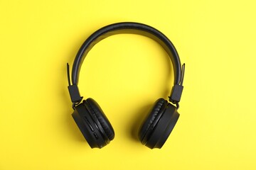 Pair of stylish black headphones on yellow background, top view