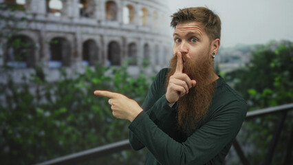 Man with long beard points finger and finger to lips for silence at roman coliseum building...