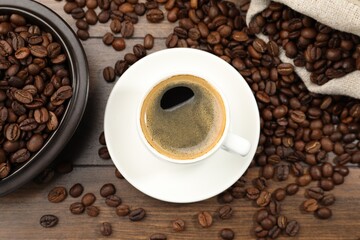 Aromatic coffee in cup and beans on wooden table, flat lay