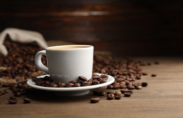 Aromatic coffee in cup and beans on wooden table, closeup. Space for text