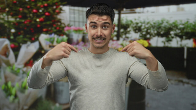 Young man happily gestures at camera in vibrant outdoor flower shop surrounded by colorful plants and decorations, capturing a lively and dynamic scene.