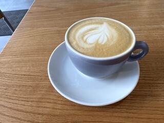 Side view of hot latte coffee with latte art in white cup on wooden table