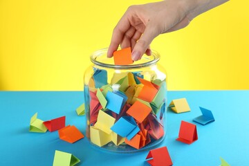 Woman taking orange paper piece from glass jar on color background, closeup