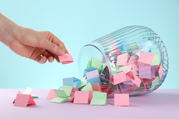 Woman taking pink paper piece from glass jar on color background, closeup