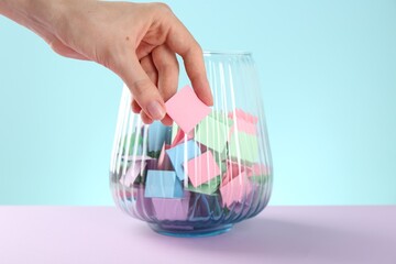 Woman taking pink paper piece from glass jar on color background, closeup