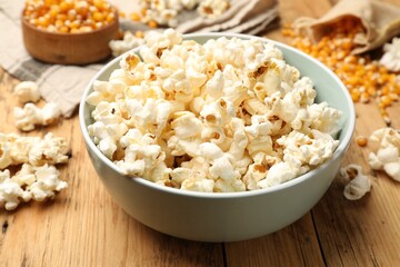 Tasty popcorn and corn kernels on wooden table, closeup