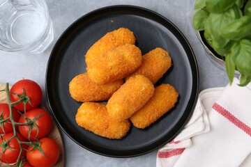 Delicious fried croquettes, glass of water, tomatoes and basil on gray table, flat lay