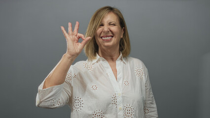 Middle age caucasian woman smiling and showing ok sign with hand in grey studio setting; confidence.