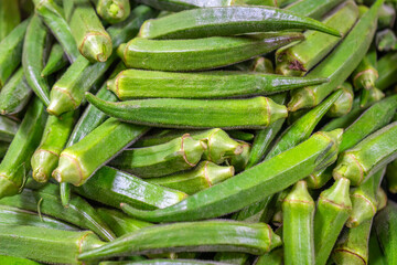 Fresh green okra pods with ridged texture stacked at a market stall, creating a vibrant natural pattern ideal for background, texture, and healthy food concepts.
