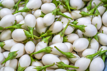 Fresh white eggplants with green calyx stacked at a market stall, creating a colorful natural pattern ideal for background, texture, and healthy food concepts.