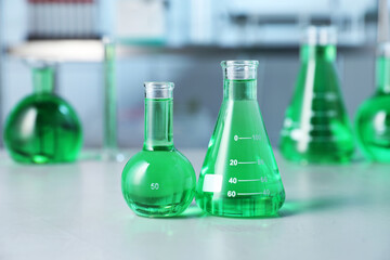 Different laboratory glassware with green liquid on light table indoors, selective focus
