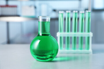 Different laboratory glassware with green liquid on light table indoors, selective focus