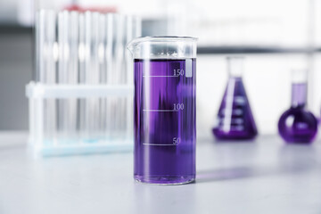 Different laboratory glassware with purple liquid on light table indoors, selective focus