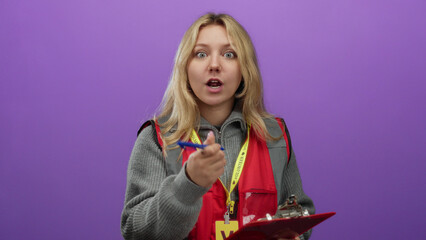 Volunteer woman writing notes on clipboard with purple background, dressed in red vest, emphasizing community service and engagement.