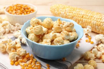 Tasty popcorn and corn kernels on light wooden table, closeup